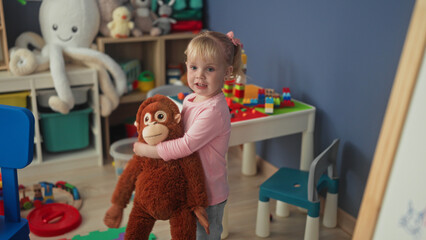 Little blonde girl hugging a large stuffed monkey with hands in a studio playroom  playful innocence. © Krakenimages.com