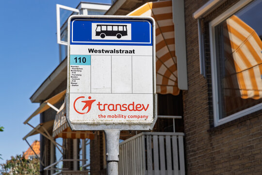 Naarden, Netherlands - July 13, 2026: A detailed view of a Transdev public transportation bus stop sign for route 110 at Westwalstraat, with residential houses in the background.