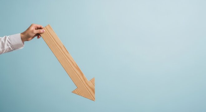 Hand holding a large wooden arrow pointing downwards against a plain light blue background