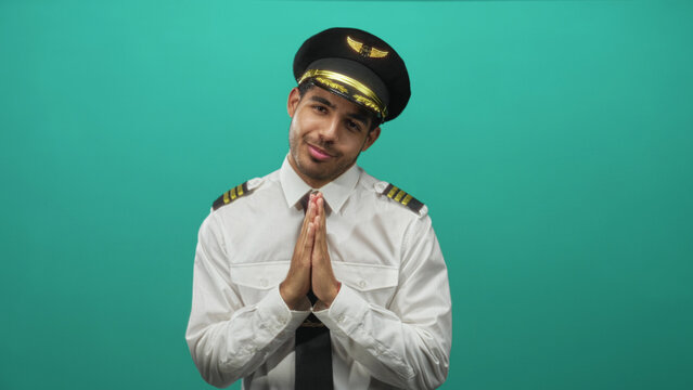 Pilot man young in white uniform shirt and captain cap with hands pressed together in pleading gesture in studio; apologetic sincerity.