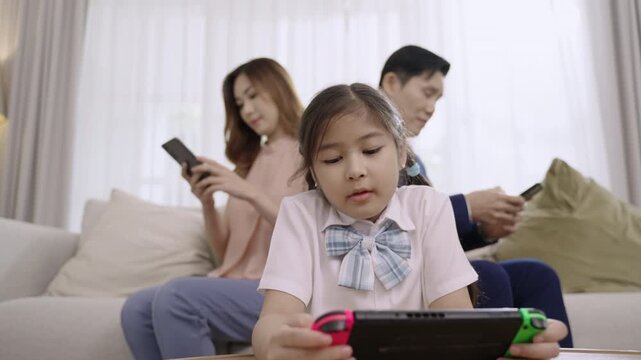 Asian family devices addicted to overusing social media to the point that they ignore their daughter and do not pay attention to each other dad and mom play phone while girl play game in living room. 