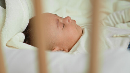 Baby boy sleeping in crib with cheek visible on white blanket inside a building  calm peaceful rest. © Krakenimages.com