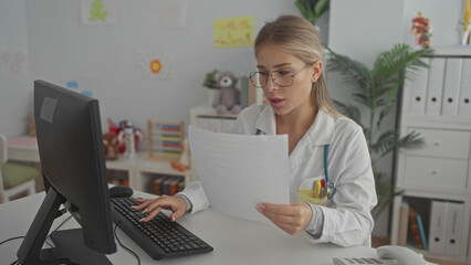 Woman doctor reading paperwork and typing with hand on keyboard at desk, reviewing medical records...