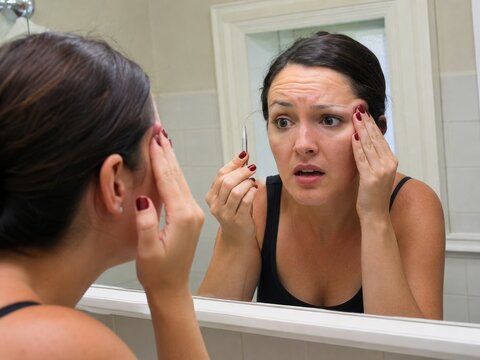 Woman upset after overplucking eyebrow in bathroom mirror