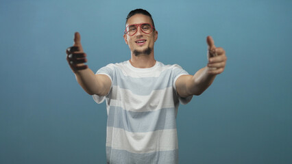 Naklejka premium Man points both index fingers to camera wearing red glasses and striped t shirt in studio; confidence invitation outreach.