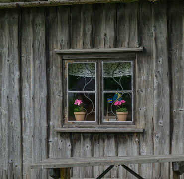 Rustic wooden cabin window with flowers and Swedish flag.