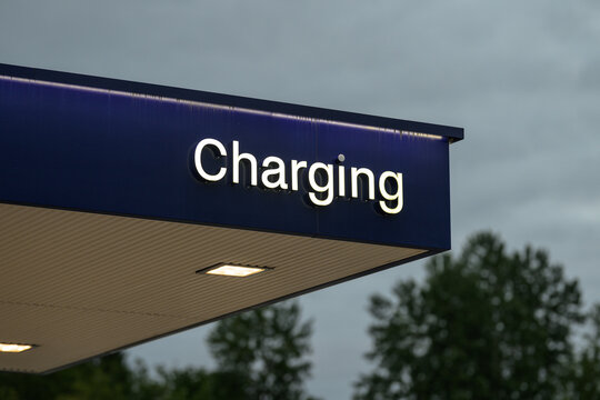 Illuminated electric vehicle charging sign under moody evening sky.