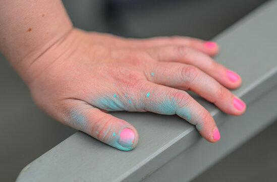 Child hand with pink nails covered in blue powder.