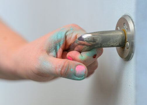 Child hand holding metal door handle with blue powder.