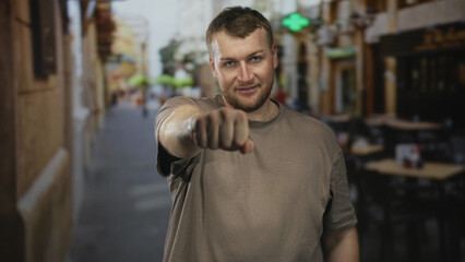 Naklejka premium Man with fist extended pointing forward on street terrace outside restaurant; confidence friendly invitation.