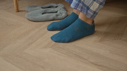 Woman slipping into grey slipper over teal sock on wooden floor in building wearing plaid pajama pants  comfort. © Krakenimages.com