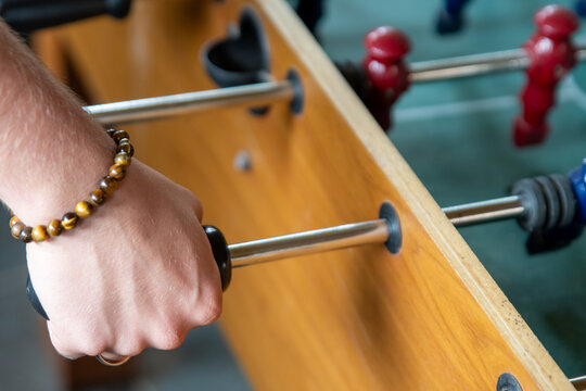 A human hand with a ring and a bracelet is holding one handle of a foosball table to play.