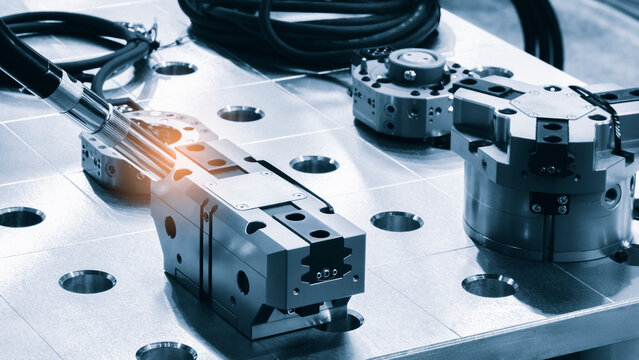 Industrial clamps and fixtures lie on a metal workbench. Black cables are coiled next to the workbench surface. tech industrial technology background