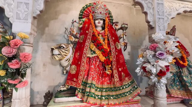Sherawali Maa seated with her lion, richly decorated with vibrant garments and flower garlands inside a Hindu temple. The goddess symbolizes courage, protection, divine feminine energy, and victory
