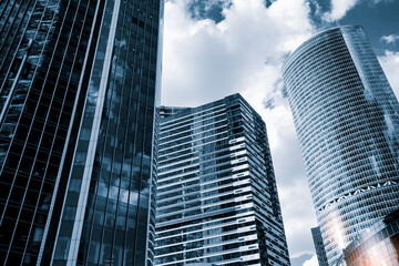 Obraz premium Tall glass skyscrapers of business offices in city reflect blue sky, clouds, and other skyscrapers. Sunlight glistens on glass surface. modern cityscape of city's business district.