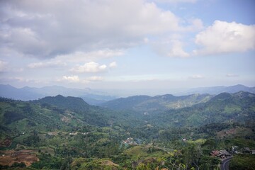 Obraz premium Panoramic scenic view of vast green hills with a majestic mountain range background under a bright cloudy blue sky.