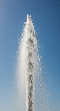 A powerful high-pressure stream of water erupts into the air, creating a dramatic mist and shimmering droplets against a bright blue sky, dynamic, powerful, sky