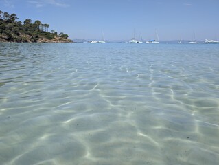 Stunning clear Mediterranean water with visible sand ripples and anchored catamarans near Porquerolles island, France. © Christel