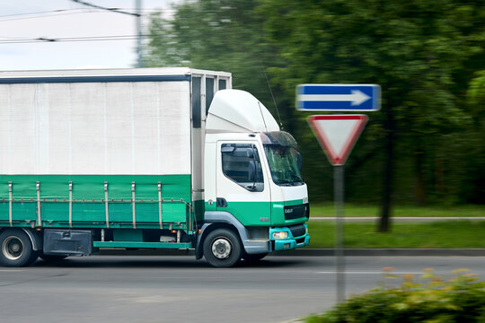 Minsk, Belarus - May 28 2021: White and green DAF LF 45.180 commercial cargo truck driving with motion blur effect past road sign on asphalt city street with green trees background.