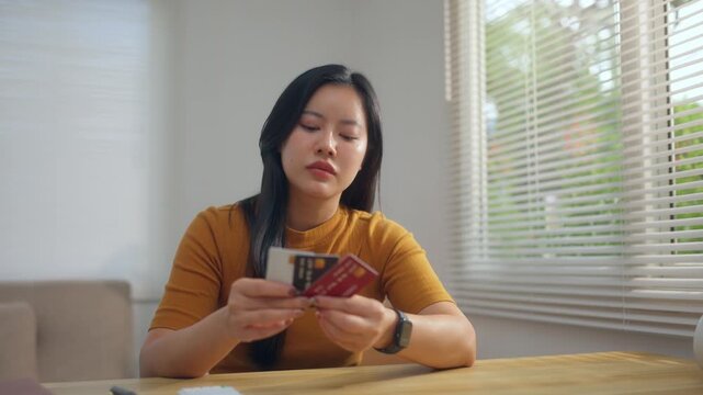 Stressed young asian woman feeling anxious about her credit card debt and overspending sitting at her home office desk