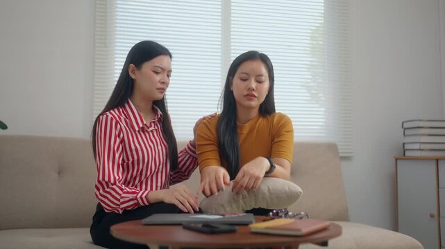 Asian woman comforting her stressed friend with credit card debt and financial problems at home