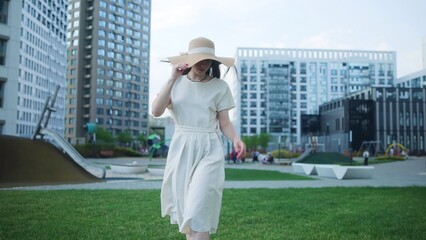 Fototapeta premium Woman walking across a city park in a light summer dress