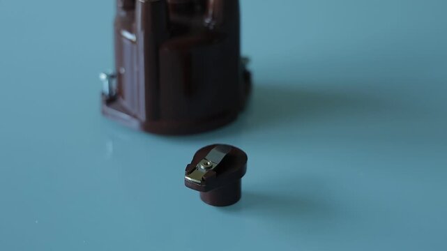 A brown plastic distributor cap with five spark plug terminals paired with its matching rotor arm, photographed on a plain gray background as automotive ignition system parts