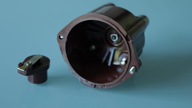 A brown plastic distributor cap with five spark plug terminals paired with its matching rotor arm, photographed on a plain gray background as automotive ignition system parts
