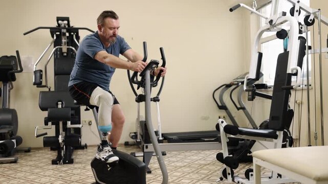Fitness equipment, Press machine, Routine equipment. At gym, man with artificial limb is actively engaging with leg press machine, other equipment in vicinity.