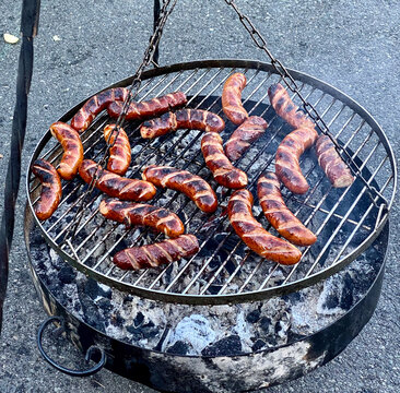 Appetizing, charred, Polish sausages on an open fire grill at an outdoor barbeque