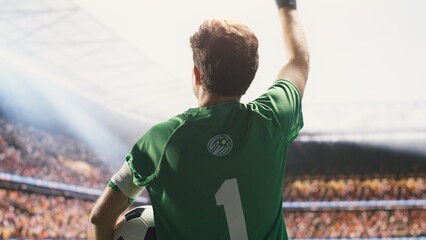 A rear perspective shows a goalkeeper saluting fans while entering the stadium with a ball under one arm, wearing a captain armband and waving toward the blurred stands before the match. © DC Studio