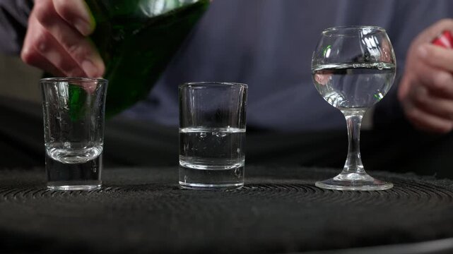 Man with glasses of alcohol. Man wringing his hands behind three glasses filled with clear alcohol, expressing anxiety, stress, and hesitation before facing an addiction problem