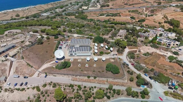 Madliena, Malta satellite communication ground station with parabolic antennas, telecom infrastructure and solar panels at an outdoor utility facility, captured in aerial view.