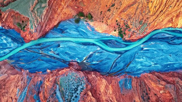Aerial view of a turquoise river winding through a red rock canyon in Xinjiang, China, creating a striking contrast of colors.
