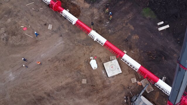Aerial view of construction site with diagonal red pipeline and active workers