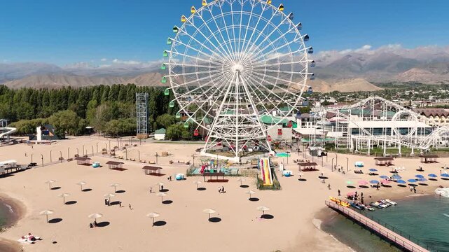 Ferris wheel by Issyk-Kul Lake with scenic mountains in the background, a popular tourist spot.