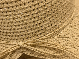 Obraz premium Close-up detail of beige woven sun hat with wide brim, decorative cord tied in bow. Natural summer fashion texture for vacation, beach accessories, handmade craft themes, copy space