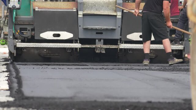Road roller compacts hot asphalt on the road. Worker focuses on guiding the machine. Black pavement spreads smoothly. Construction workers work hard. Ideal for road-building projects