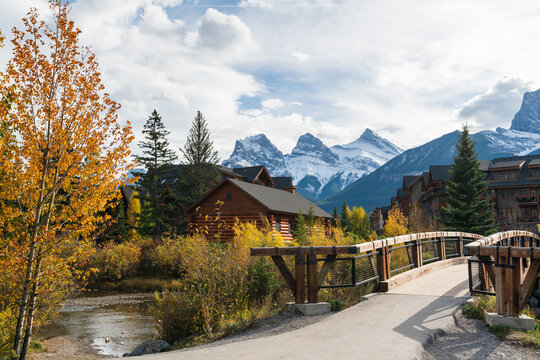 Town of Canmore in fall season. Alberta, Canada. Canmore Opera House at Spring Creek beside the wooden boardwalk bridge. The Three Sisters trio of peaks in the background.