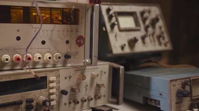 Close view of stacked vintage electronic test instruments on repair bench with warm directional light, metal faceplates, colored sockets, cables, knobs, and shallow focus