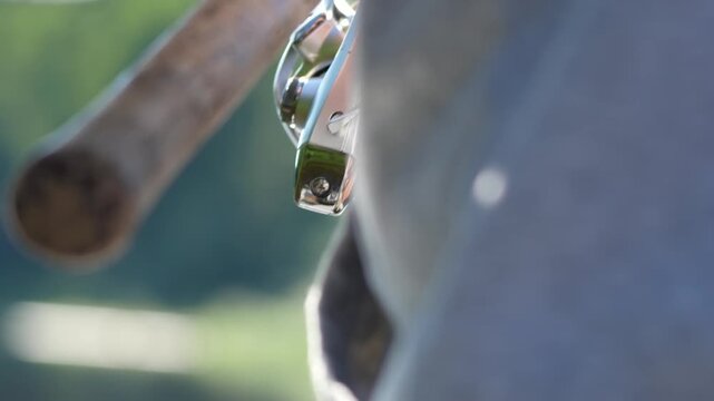 Worn wooden handle is visible in close-up. Hand grips it firmly. Gray fabric surrounds the handle. Blurred greenery forms the background. Ideal for sports or outdoor gear themes