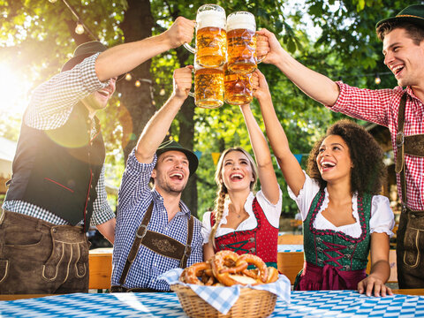 Group of happy friends in traditional Bavarian dress cheering with beer mugs at Oktoberfest