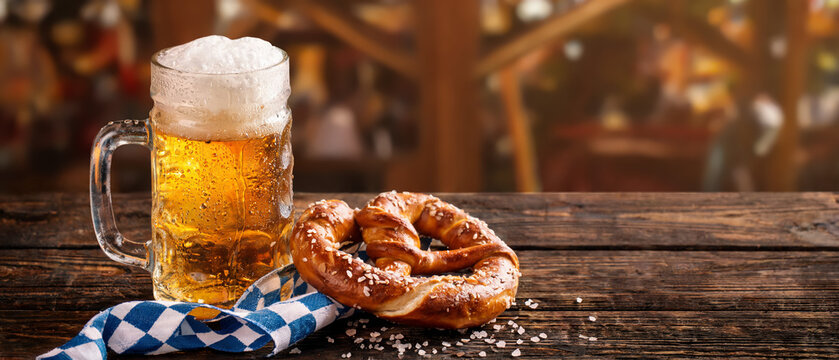 German soft pretzel with glass of foaming beer on rustic table, Oktoberfest banner copy space