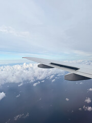 Fototapeta premium Scenic passenger view from an airplane window looking over the aircraft wing in flight. Beautiful white cumulus clouds spread below and across a blue sky daytime horizon.