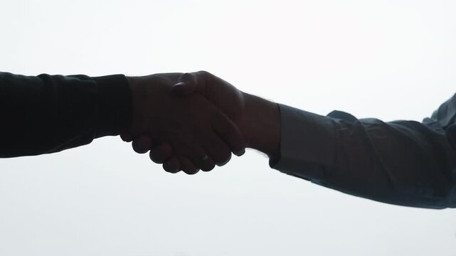 Close-up handshake silhouette centered against bright white background showing firm professional grip between two forearms in clean studio composition with strong contrast