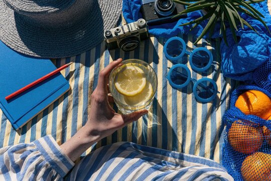 Person holds lemon water on striped blanket with vintage camera & fruit