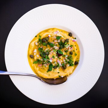 Traditional Greek fava dip with capers, red onion and parsley in white bowl