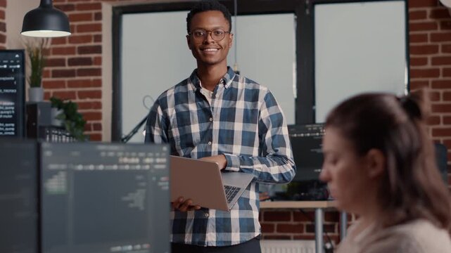 African American software developer writes programming code on a portable computer at a desk, connecting laptop workflow with software engineering, inside a professional software studio.