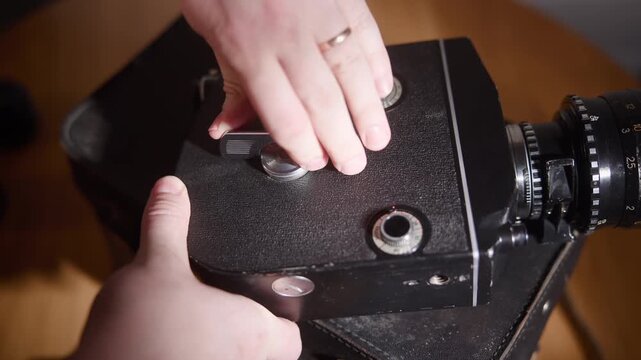 Hands adjusting chrome winding knob and lever on vintage camera top plate with textured black leather surface, warm directional light, close-up detail, tactile mechanical control