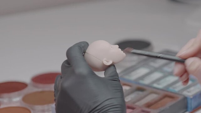 Close-up of an artist carefully painting the face of a female PLA ball jointed doll using a fine brush during the customization process.
